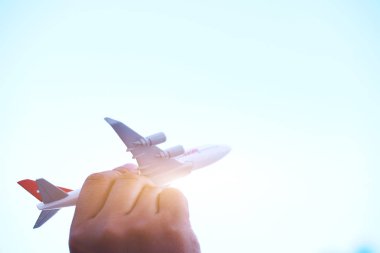 Gün batımında bulutların üzerinde uçan minyatür oyuncak bir uçak tutan genç Asyalı. Yazın seyahat ve seyahat. Kopya uzayı olan uçakla.