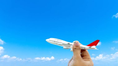 Gün batımında bulutların üzerinde uçan minyatür oyuncak bir uçak tutan genç Asyalı. Yazın seyahat ve seyahat. Kopya uzayı olan uçakla.