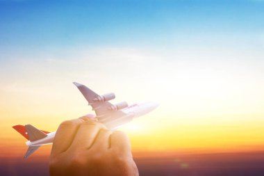 Gün batımında bulutların üzerinde uçan minyatür oyuncak bir uçak tutan genç Asyalı. Yazın seyahat ve seyahat. Kopya uzayı olan uçakla.