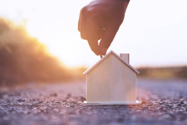 Güneş batımında ahşap ev modeline altın sikke koymak. Para biriktirmek ve işletme finans kavramını geliştirmek..