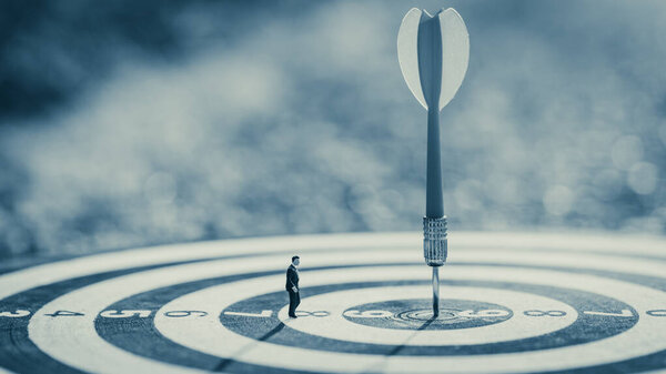 Businessman standing lookup red dart arrow hitting target centre dartboard on sunset background. Business targeting and focus.