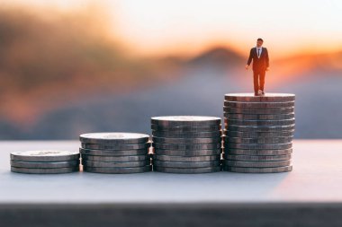 Gün batımının altında para yığını üzerinde duran minyatür işadamını kapatın. İş finansmanı büyüme kavramı.