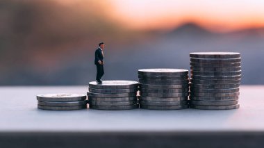Gün batımının altında para yığını üzerinde duran minyatür işadamını kapatın. İş finansmanı büyüme kavramı.