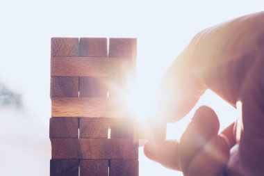 İş planı, strateji ve risk kavramı. İş adamı gün batımının altında kuleye tahta blok yerleştiriyor..