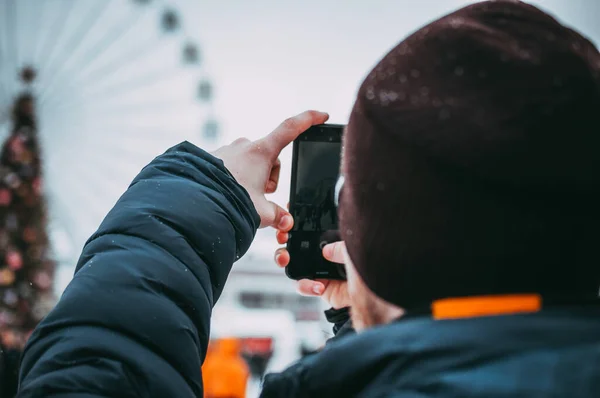 Closeup image of male hands using smartphone by day on the street. The guy photographs a Christmas tree and a Ferris wheel. concepts of social networks, photography.