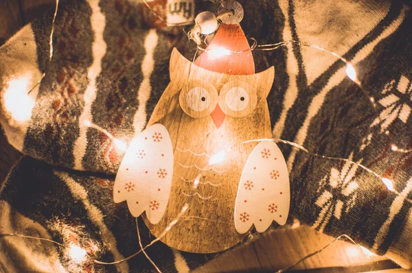 wooden owl Christmas garland lies on a fabric, illuminated by LED garland. Christmas holidays concept.