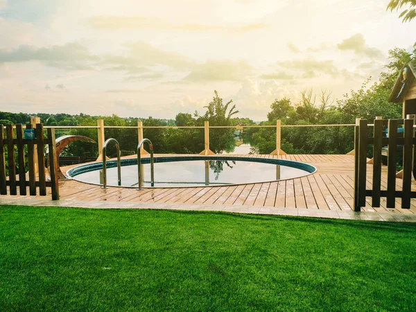 Piscina con escaleras y terraza de madera en el hotel. Vista de la piscina y el río desde un prado verde. El concepto de la llegada del verano y la natación . —  Fotos de Stock