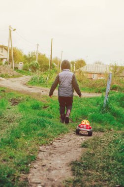 Mavi yelek ve lastik çizmeli bir çocuk çamurda bir daktilo taşıyor. Çocuk yaz yağmurundan sonra dışarı çıkıyor. Tasasız çocukluk kavramı..