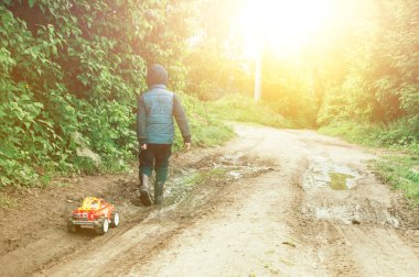 Mavi yelek ve lastik çizmeli bir çocuk çamurda bir daktilo taşıyor. Çocuk yaz yağmurundan sonra dışarı çıkıyor. Tasasız çocukluk kavramı..