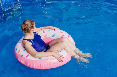 Yaz tatili. Kız mavi bir havuzda donut şeklinde lastik bir halkanın üzerinde oturuyor. Şişme yatakta dinlenme zamanı. Aile tatili için suda eğleniyorum. Deniz tatil köyü. Boşluğu kopyala.