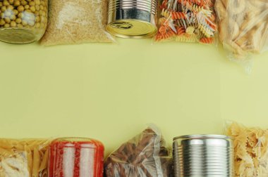 Sarı arka planda makarna, pirinç, kurabiye, domates sosu, bezelye ve konserve yiyeceklerden oluşan bir set. Yemek teslimatı, bağış konsepti. Yiyecek kaynaklarını karantinaya alın. Boşluğu kopyala