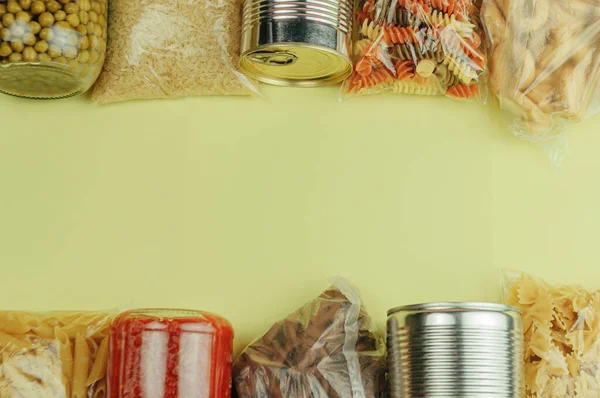 Sarı arka planda makarna, pirinç, kurabiye, domates sosu, bezelye ve konserve yiyeceklerden oluşan bir set. Yemek teslimatı, bağış konsepti. Yiyecek kaynaklarını karantinaya alın. Boşluğu kopyala