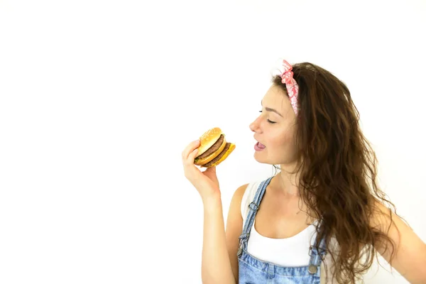 güzel kız hipster iştah ile hamburger yiyor. Beyaz bir arka plan üzerinde model