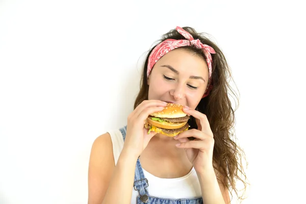 güzel kız hipster iştah ile hamburger yiyor. Beyaz bir arka plan üzerinde model