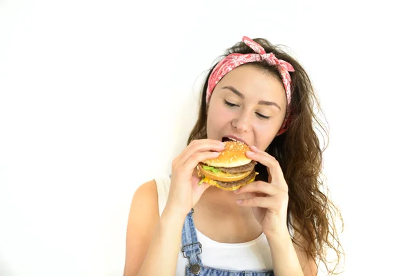 güzel kız hipster iştah ile hamburger yiyor. Beyaz bir arka plan üzerinde model