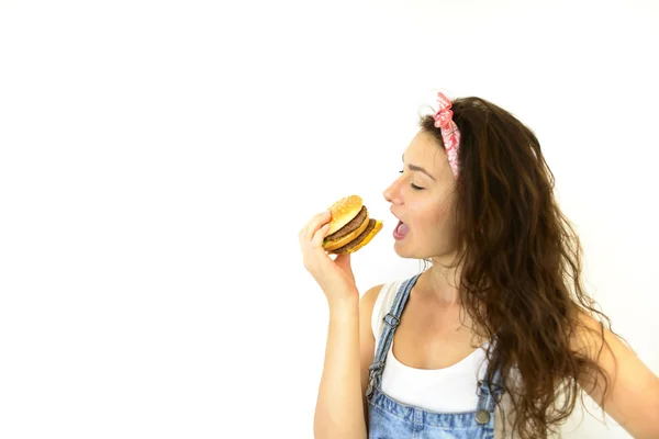 güzel kız hipster iştah ile hamburger yiyor. Beyaz bir arka plan üzerinde model