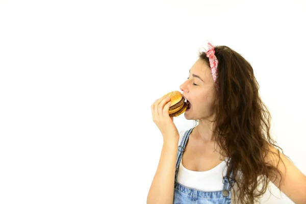 güzel kız hipster iştah ile hamburger yiyor. Beyaz bir arka plan üzerinde model