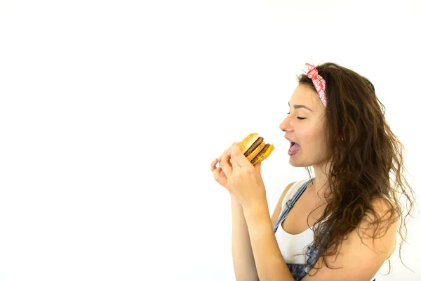 Beautiful girl hipster with appetite bites burger. Model on a white background — Stock Photo, Image