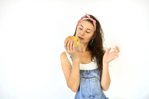 Linda garota hipster está segurando um hambúrguer e vai comê-lo. Modelo sobre um fundo branco — Fotografia de Stock