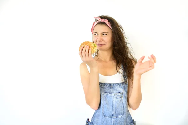 güzel hippi kız hamburger tutuyor ve yüzler yapın. Beyaz arka plan üzerinde izole modeli