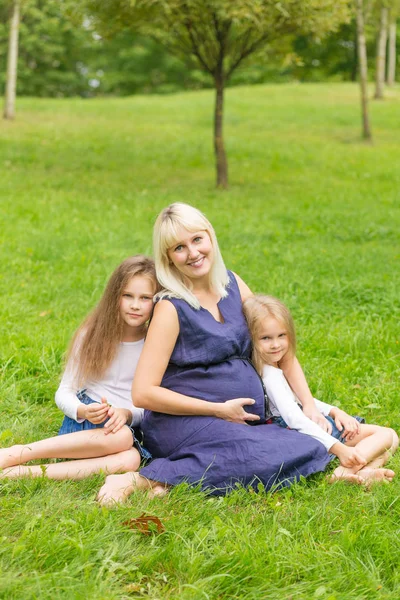 Mladá těhotná matka se svými dcerami v parku — Stock fotografie