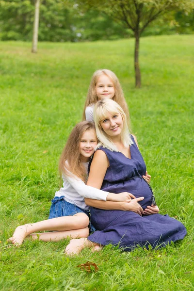 Молодая беременная мать с дочерьми в парке — стоковое фото