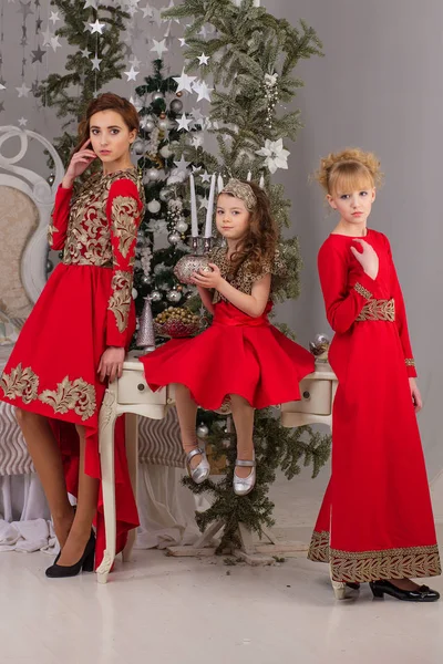 Tre flickor i en röd kväll klä granen. — Stockfoto