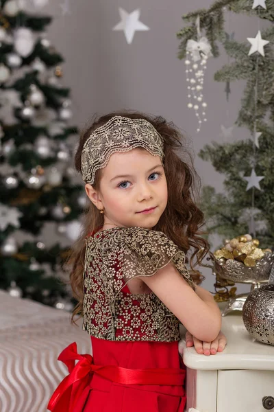 Kleines schönes Mädchen in einem roten Abendkleid den Weihnachtsbaum. — Stockfoto