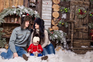 Bir Noel ağacın altında oturup kürk şapka çocuk ile genç Çift.