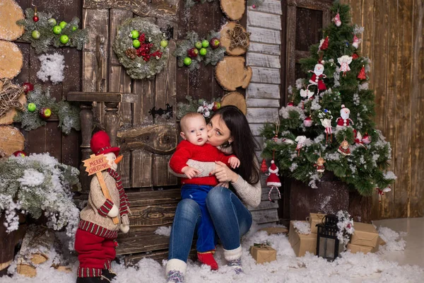 Giovane madre con bambino seduto su un albero di Natale . — Foto Stock