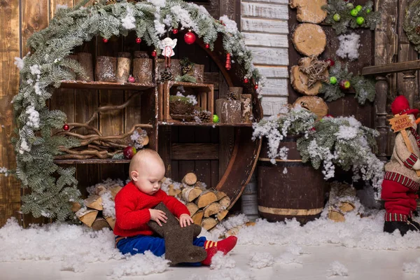 Bambina in un maglione rosso lavorato a maglia sta giocando con gli stivali . — Foto Stock
