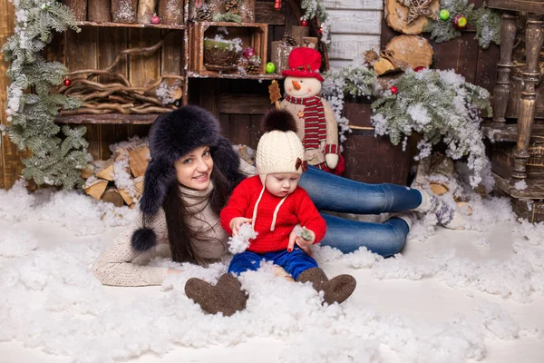 Giovane madre con bambino in cappelli di pelliccia seduta in un albero di Natale . — Foto Stock