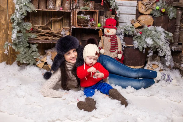 Giovane madre con bambino in cappelli di pelliccia seduta in un albero di Natale . — Foto Stock