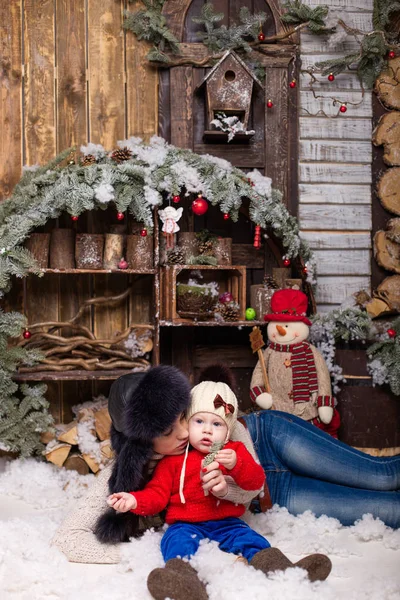 Giovane madre con bambino in cappelli di pelliccia seduta in un albero di Natale . — Foto Stock