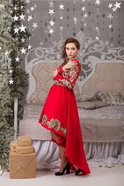 Красивая девушка в красном длинном платье у елки — стоковое фото