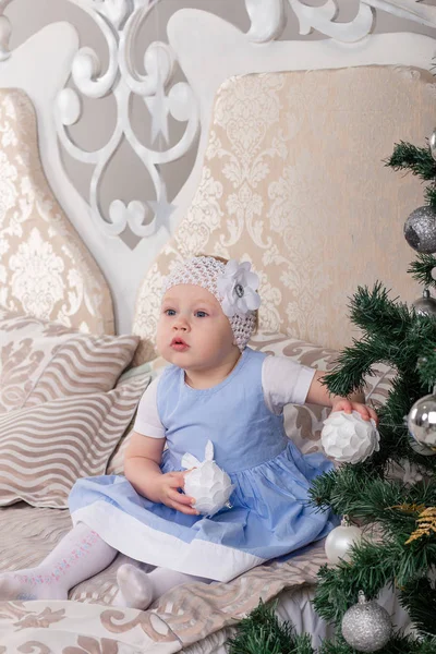 Το μικρό κορίτσι σε ένα μπλε φόρεμα για το χριστουγεννιάτικο δέντρο στο κρεβάτι — Φωτογραφία Αρχείου