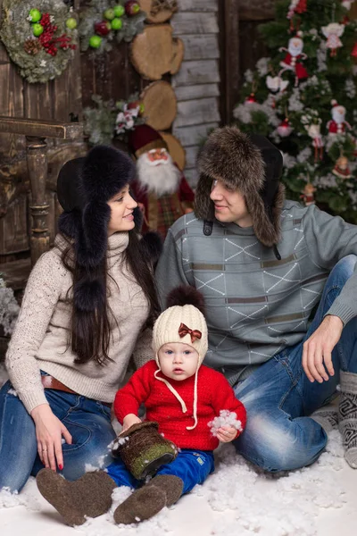 Coppia giovane con bambino in pelliccia seduto su un albero di Natale . — Foto Stock