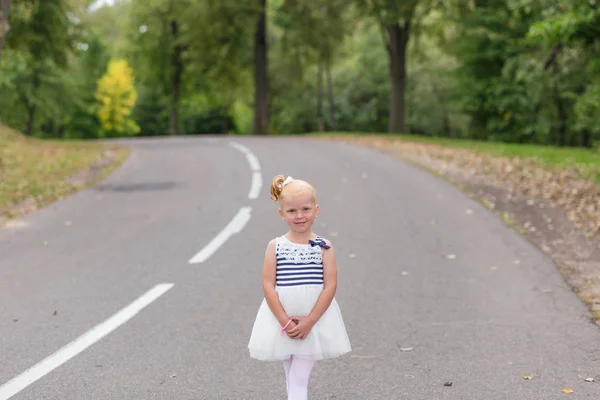 Una linda niña en un hermoso vestido y zapatillas de deporte jugando en — Foto de Stock
