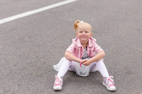 Una linda niña en un hermoso vestido y zapatillas de deporte jugando en —  Fotos de Stock