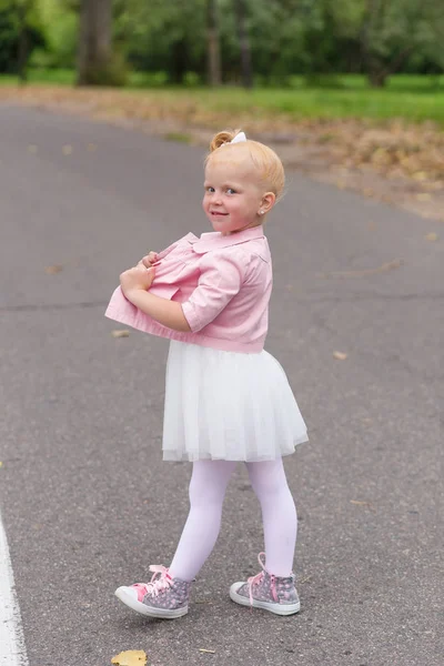 Милая маленькая девочка в красивом платье и кроссовки играют на — стоковое фото