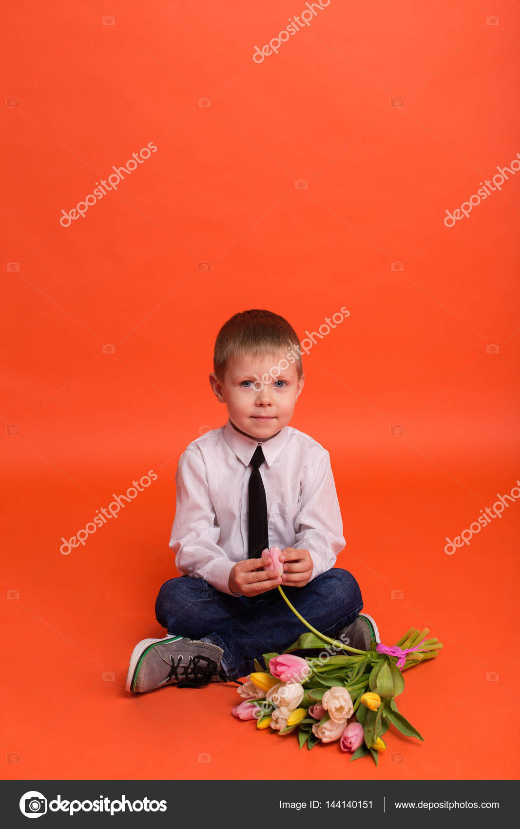 Little boy with flowers posing in the studio on a red background Stock