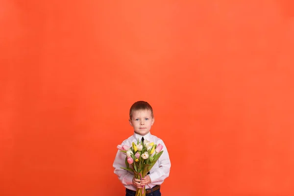 Petit garçon avec des fleurs posant en studio sur un fond rouge — Photo