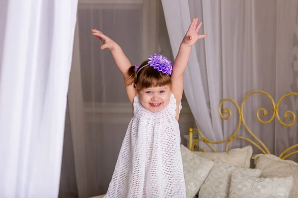 Ένα μικρό κορίτσι σε ένα λευκό πλεκτό φόρεμα, Περιποιηθείτε τον εαυτό σας σε ένα κρεβάτι — Φωτογραφία Αρχείου