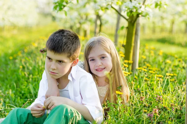 Un niño y una niña descansan en un jardín floreciente en primavera. — Foto de Stock