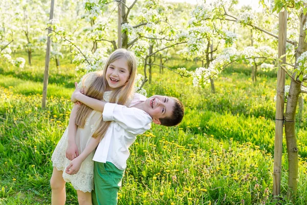 Un niño y una niña descansan en un jardín floreciente en primavera. — Foto de Stock