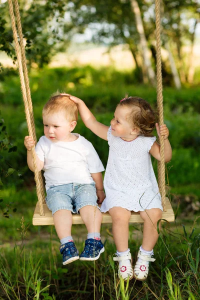 Dos niños pequeños están montando en un columpio al aire libre — Foto de Stock