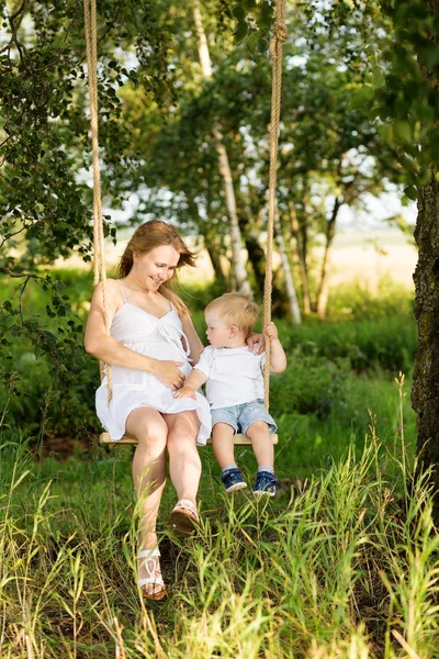 Маленький хлопчик з вагітною матір'ю сидить на гойдалці . — стокове фото