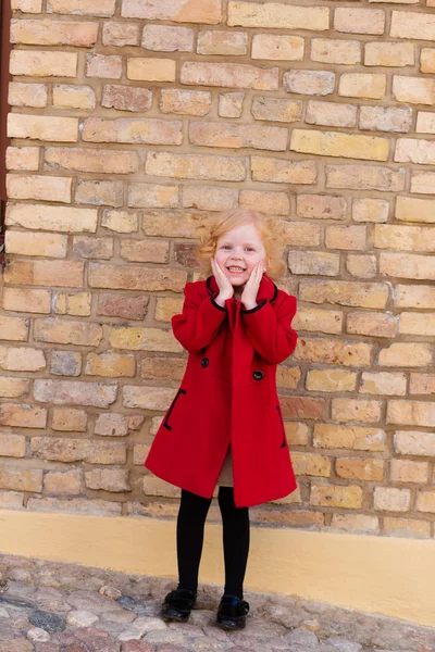 Portrait of a beautiful little girl with red hair in a red coat — Stock Photo, Image