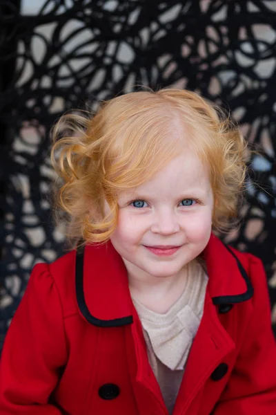 Portrait of a beautiful little girl with red hair in a red coat — Stock Photo, Image