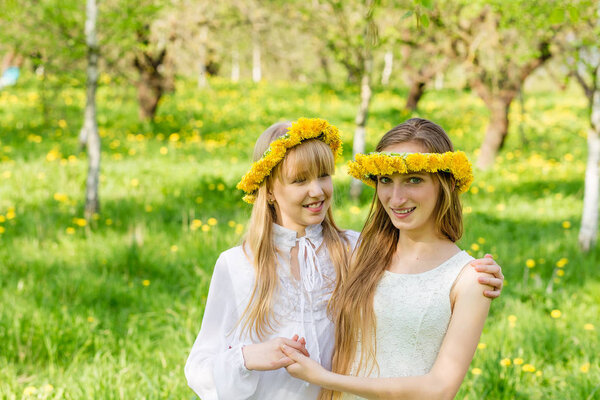 Girlfriends are standing with wreaths of dandelions on their hea